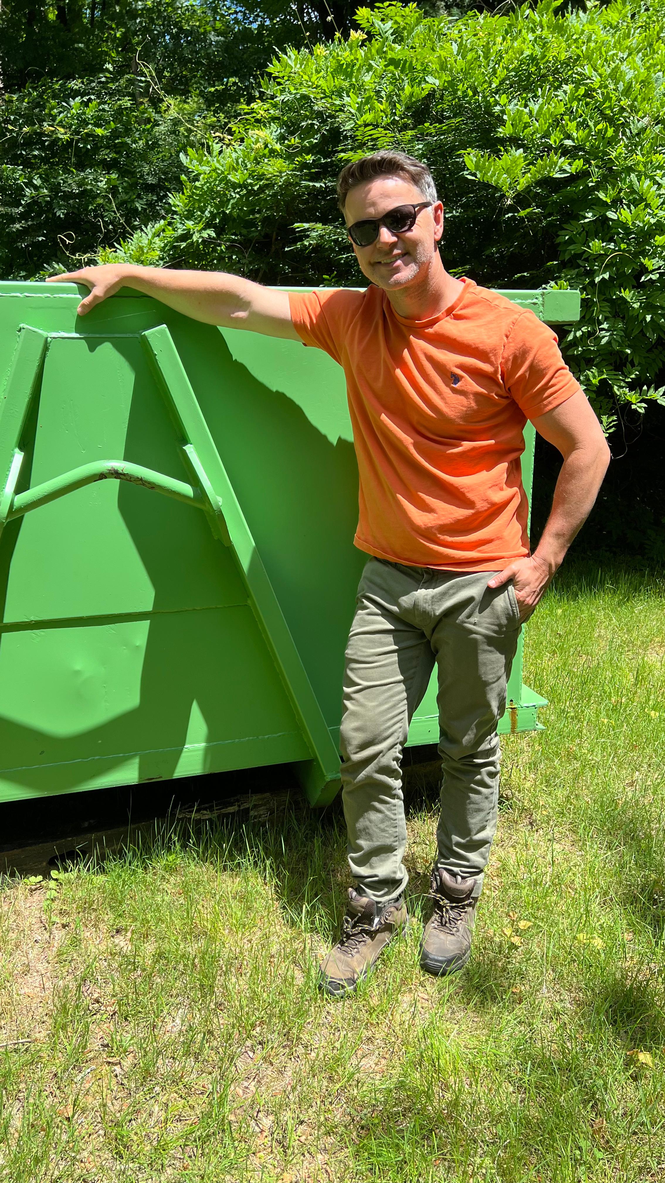 Owner standing next to green dumpster